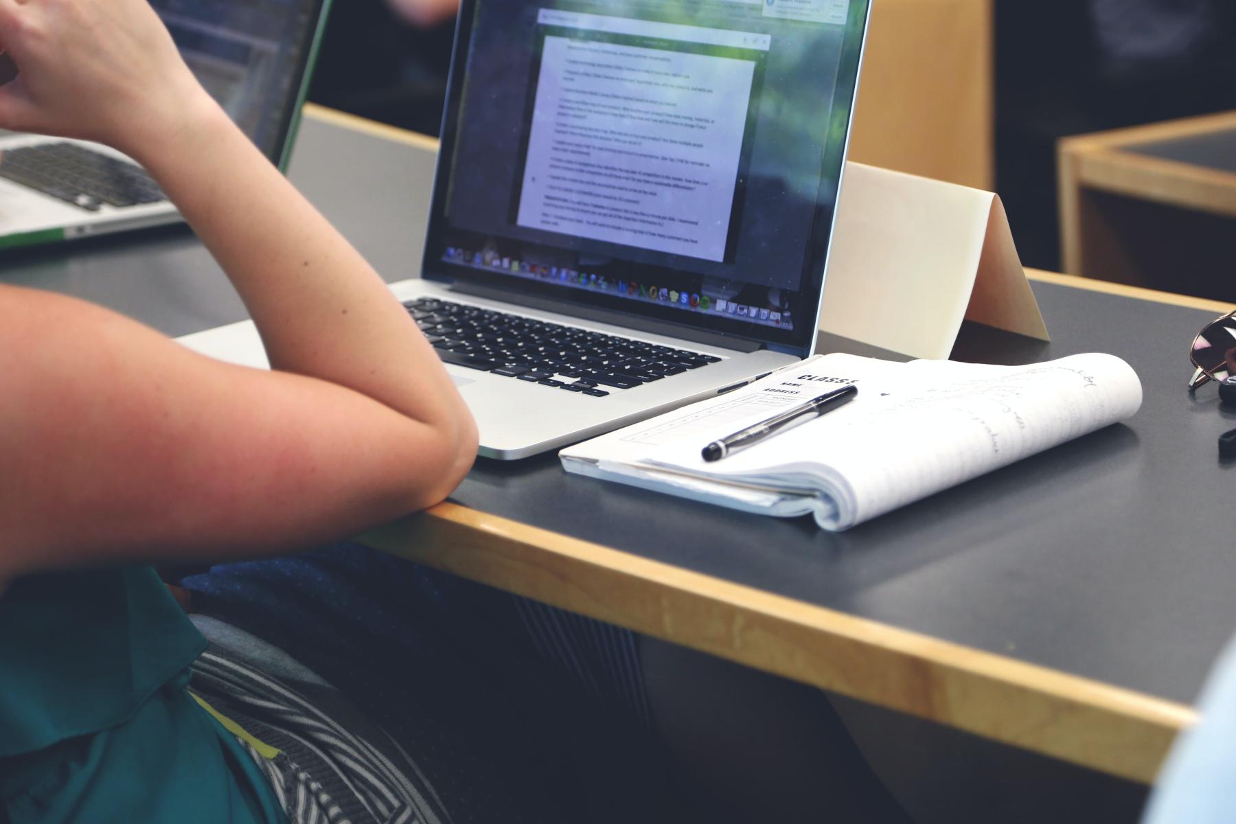 Student works on laptop with a notebook and pen next to them